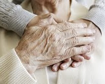Photo of an elderly person holding another persons hands across the chest, comforting